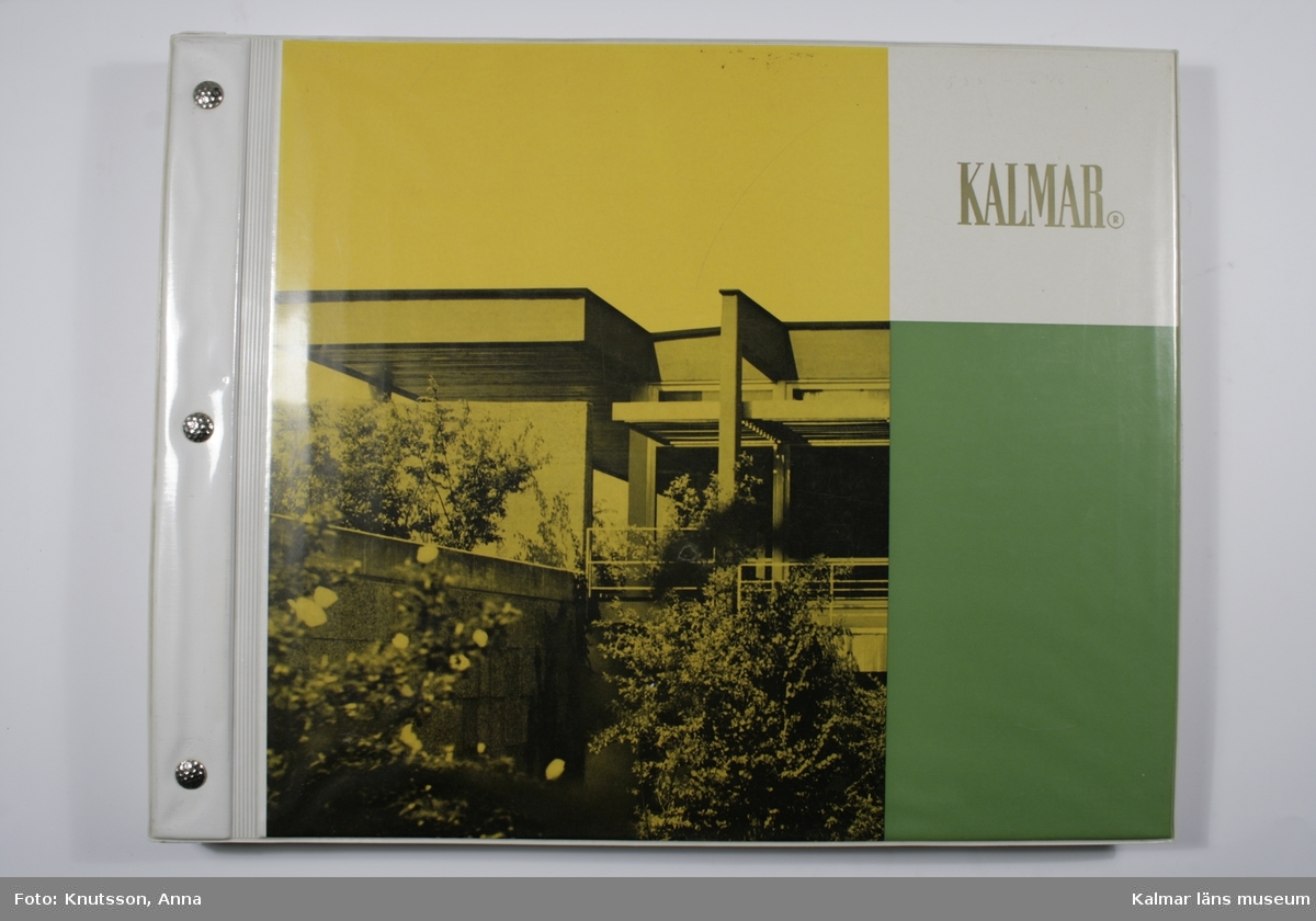 KLM 33296. Tapetkatalog. Vit, gul och grön pärm i plast med fotografi av en byggnad. Tapetkatalog för Kalmar Nya Tapetfabrik, innehåller många olika prover av tapeter från 1970-talet.