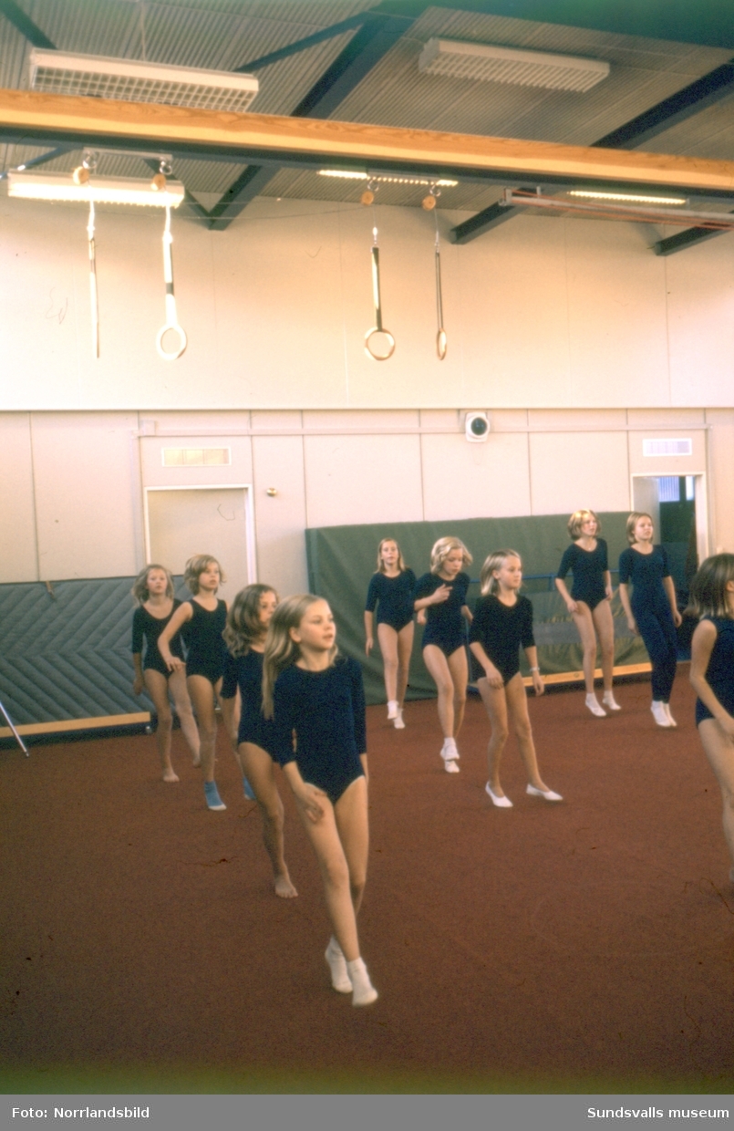 Gymnastiklektion på Nackstaskolan. Större delen av flickorna har tidstypisk klädsel i form av sockiplast och mörkblå gymnastikdräkt.