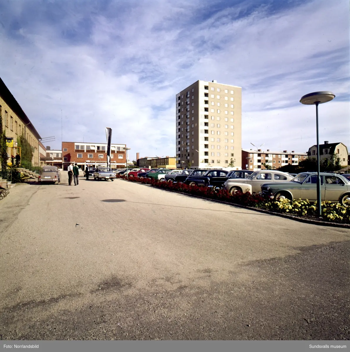 Skönsbergs centrum fotograferat från parkeringen utanför posten mot torget utanför Folkets hus med konstverket Spiral reflex, höghuset, ABE foto ateljé, Borgs Livs, Konsum.
