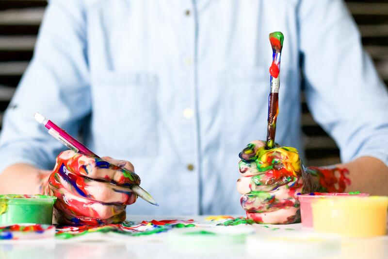 Bildet viser en mann som maler og tegner, med masse malingssøl på hendene