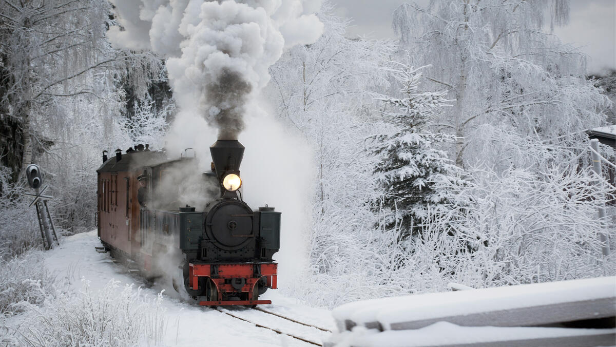 Damplokomotiv med vogner i snødekt landskap.