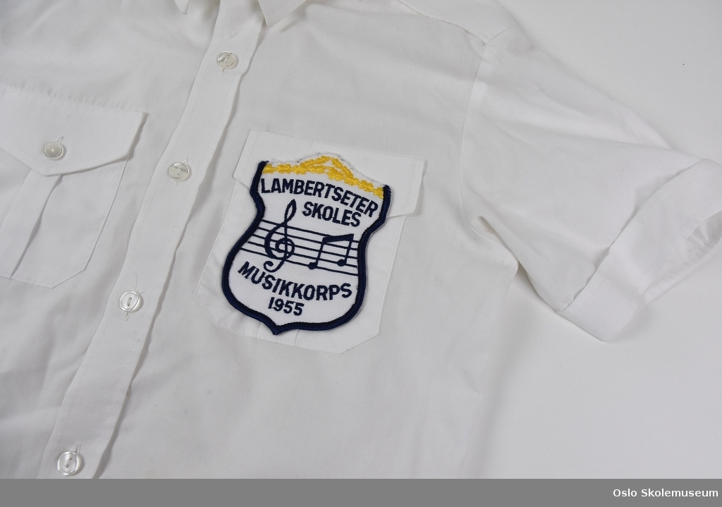 Hvit skjorte fra Lambertseter skoles musikkorps til barn. Skjorten har korpsets emblem.
