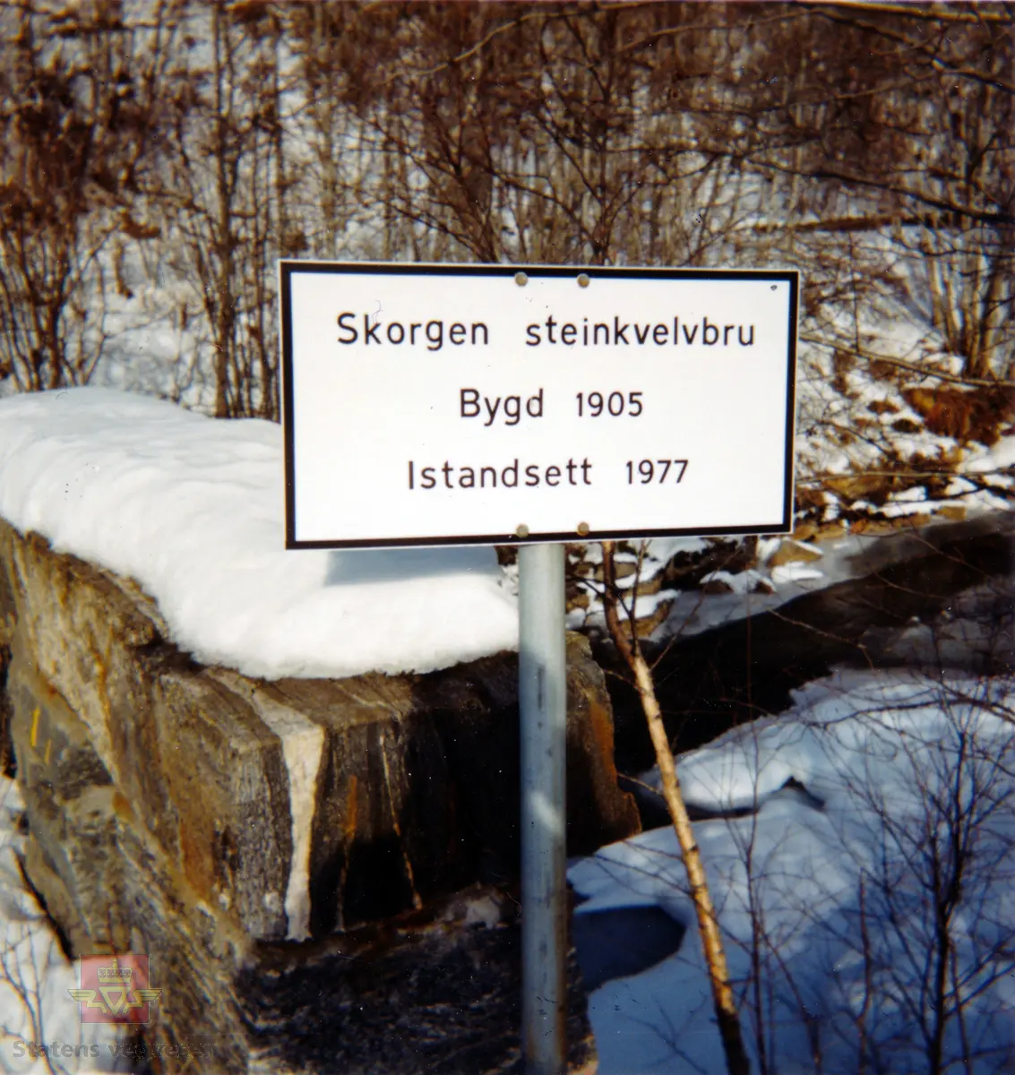 Skilt ved Skorgen steinhvelvbru av hogget stein som ble bygd i 1905 og restaurert i 1977.

På skiltet står: "Skorgen steinkvelvbru Bygd 1905 Istandsett 1977".

Merking bak på bilde: "Foto: E. Bakke 1988".

