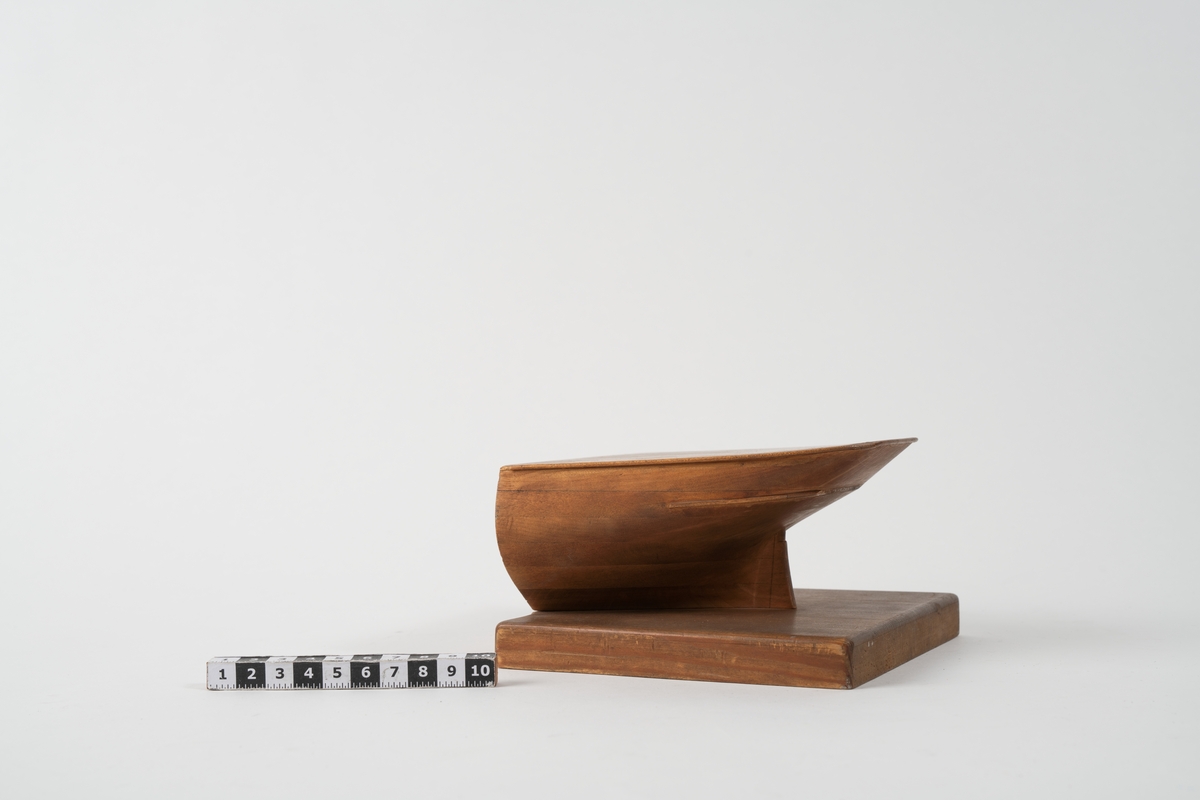 Blockmodell av akterstäv av skeppsgossebriggen Najaden. Av trä, fastsatt till platta av trä. Märkning med blyerts: Modell Najaden Briggen.