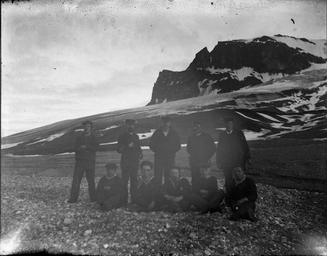 Fem män sitter framför fem stående på en strand någonstans på Spetsbergen. Alla bär flottans uniform och bland stående är åtminstone tre officerare. Stående som tvåa från vänster är kapten Hamilton, fyra och femma sannolikt löjtnanterna Arnelius och Lagercrantz