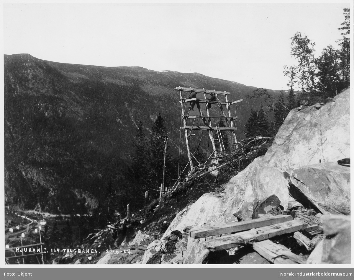 Anleggsarbeidere sittende i trekonstruksjon oppe i fjellsiden bygget til taubanen mellom Vemork - Våer.