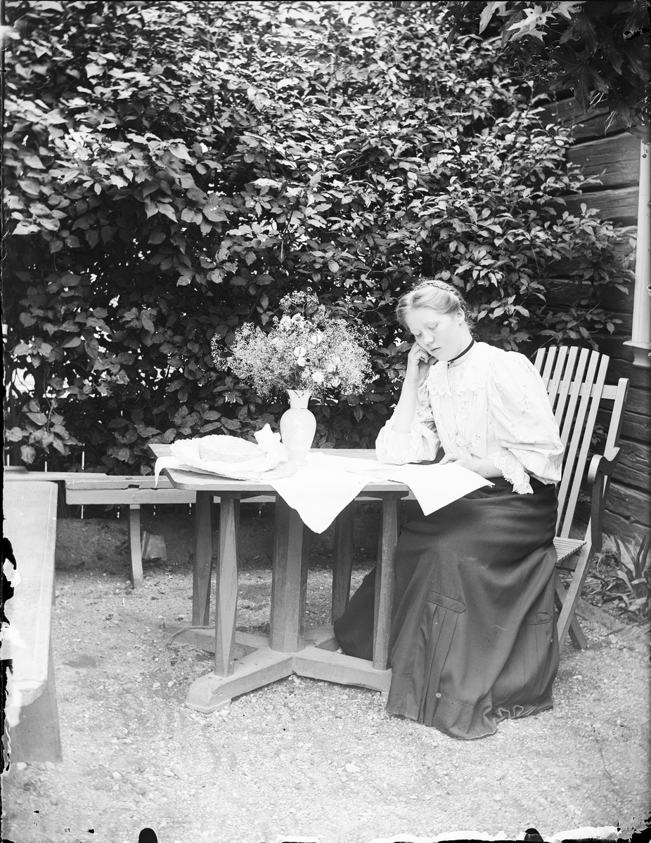 Ruth Skötsner sitter ute vid bordet och läser, Östhammar Uppland