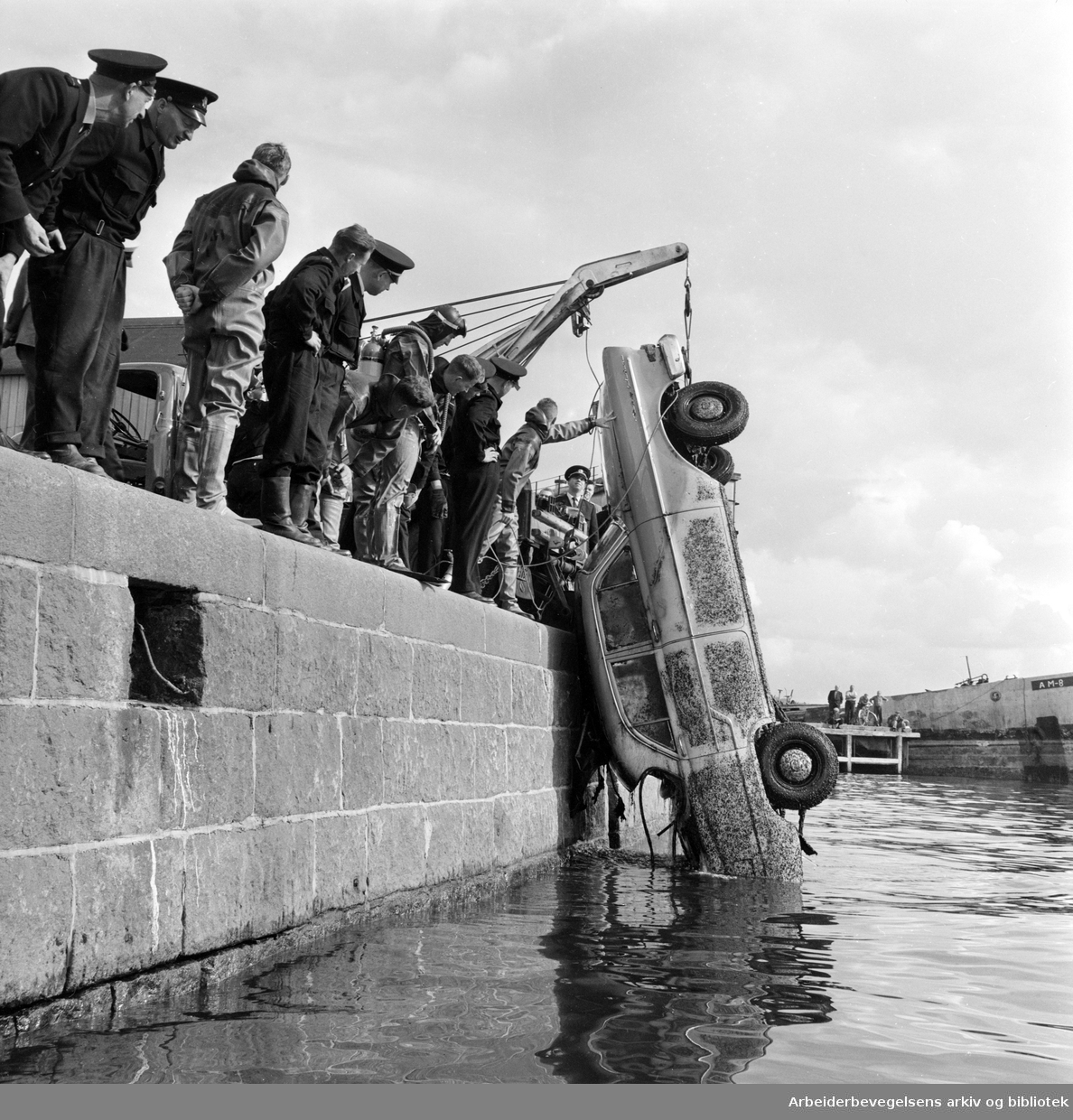 Dykkere fra Oslo Brannvesen heiser i land et bilvrak ved kaia på Vippetangen. August 1962.