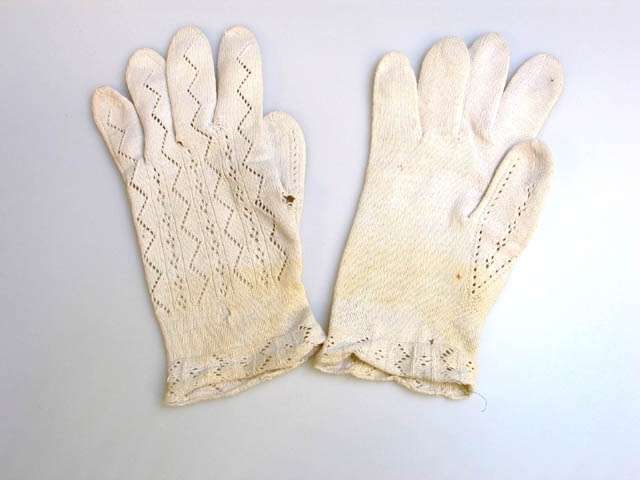 Ett par fingervantar i vitt bomullsgarn, mönsterstickade. Dekorerade med sick-sackgående hålsändar som fortsätter ut på fingrarna. Handlinningens bård med samma mönster. Vantarna har varit utställda i basutställningen "I barnaminne" på Landskrona museum. Utställningen stod mellan 1989 och 2007.