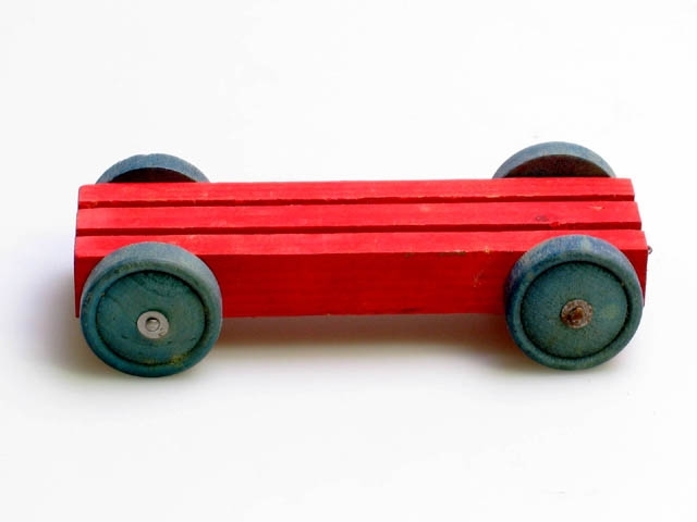 Träbil eller vagn. Rödmålad träbit med två skåror i och med blåmålade hjul.