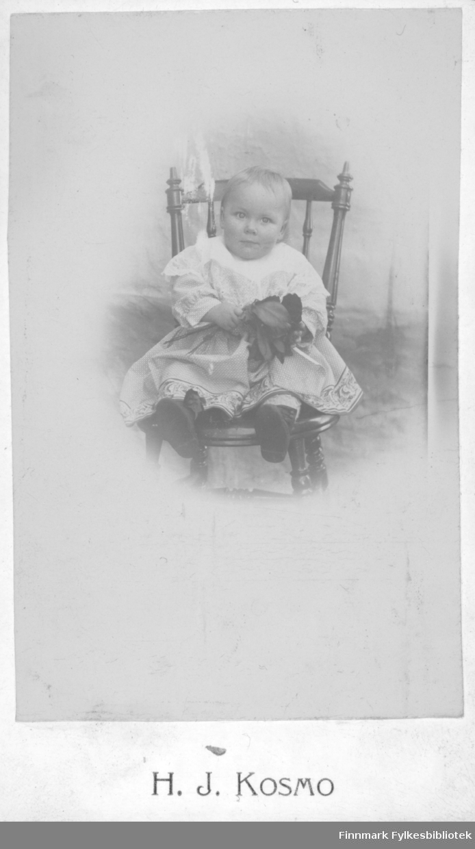 Fotoatelierbilde av ei lite jente av Hans Jensen Kosmo. Han var fotograf og tok bilder på Fuske i Stokke fra omkring 1895 til 1900.