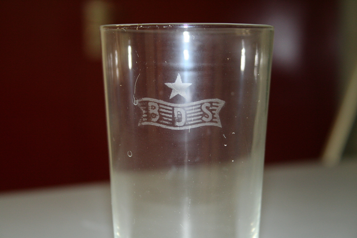 Drikkeglass i transparent glass, med innskrift BDS og ei stjerne på siden.