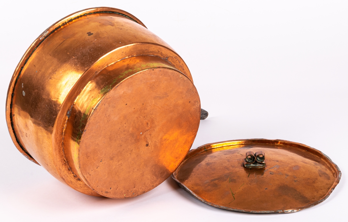 Kastrull, koppar, med lock och skaft.
Mått:
a) h 11.5cm, diam, 19cm (kastrull).
b) diam 8,5 cm (lock).
Från 1800-talets senare del.
