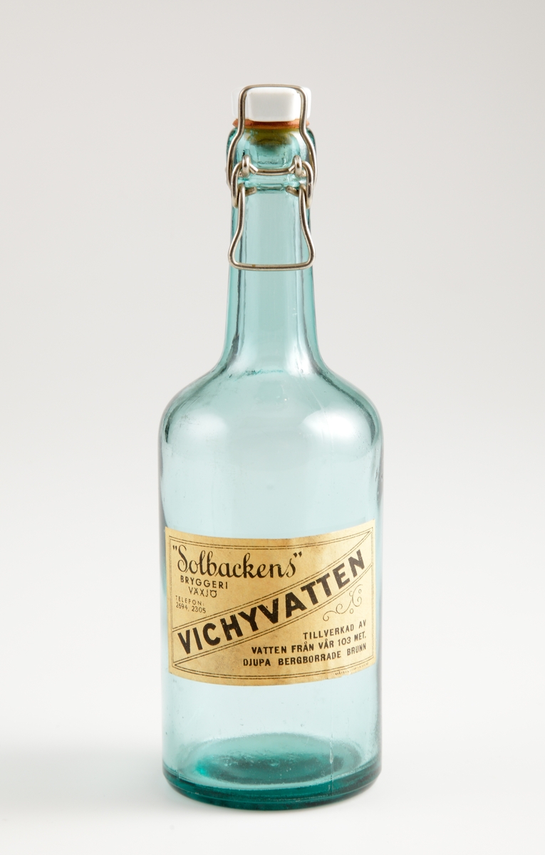 Grön flaska, med patentkork, för vichyvatten. Flaskan tillverkad på Årnäs glasbruk 1940. Vichyvatten från Solbackens bryggeri i Växjö. Etikett: ""Solbackens" // BRYGGERI // VÄXJÖ // VICHYVATTEN // TILLVERKAD AV // VATTEN FRÅN VÅR 103 MET. // DJUPA BERGBORRADE BRUNN"
