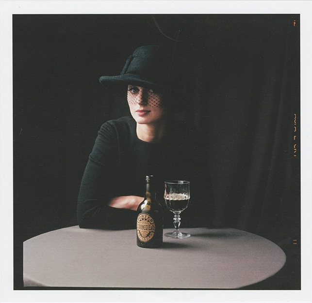 Reklamfoto för marknadsföring av Carnegie Porter.
Halvkroppsporträtt. Kvinna sitter vid bord. Hon har på sig en svart överdel och svart hatt med svart flor framför ansiktet. Hon lutar armarna mot bordet. Framför henne står en flaska Carniege Porter och ett glas på fot fyllt med öl.
