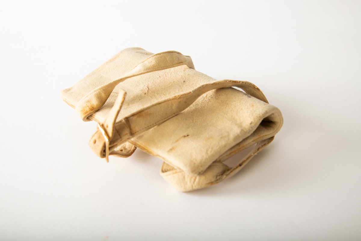 Rektangulær pose med to lommer,  lukket med  glidelås, den ene foret med tynt lerret. Lang rem i samme lyse skinn, til å ha rundt halsen. I nederste lomme lå en sixpence,  Georg V, 1926.