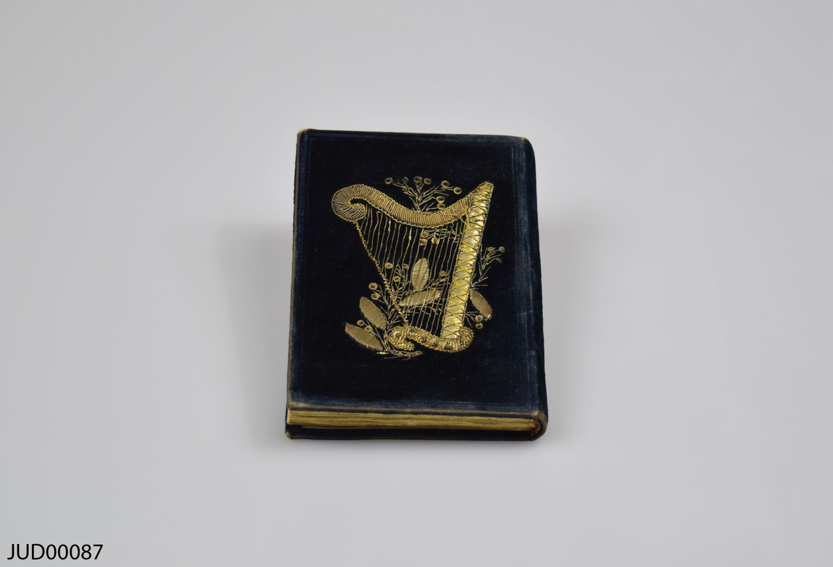 Bönbok med mörkblått sammetsomslag. Dekorationer utförda med guldtråd i form av initialerna LS på ena sidan, och en harpa på andra sidan.