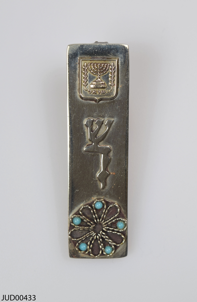 Liten mezuza tillverkad av silver. Dekorerad med staten Israels emblem samt blomma med turkosa stenar.