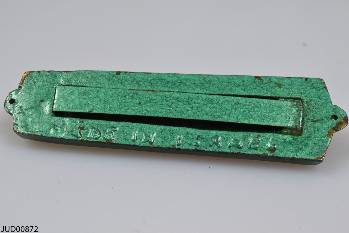 Mezuza tillverkad av metall. Målad grön med guldfärgade detaljer på framsidan.