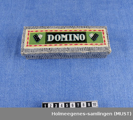 Esken er trukket med papir i svart og hvitt slangeskinnmønster. På lokket er et bilde av dominobrikker i hvitt og svart, med ordet DOMINO i midten.