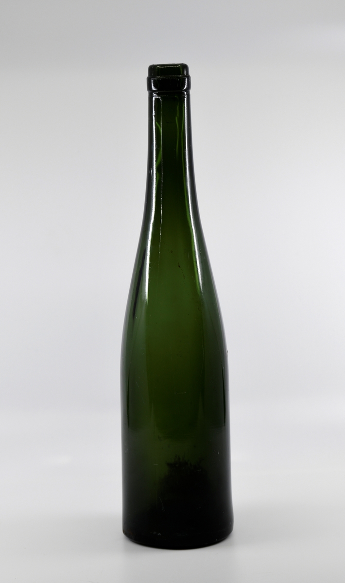 En grønn glassflaske med lang og slank hals. Den er blåst i form.