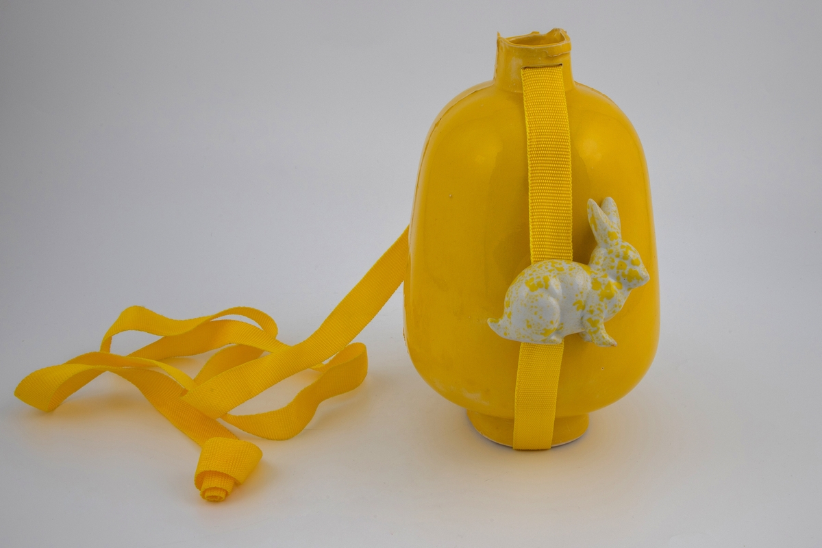 Krukken i støpt porselen med monokrom gul glasur. Den har et spor i halsen hvor det er festet en gul nylontrå som fester en hvit og gulflekket hare til krukkens side.