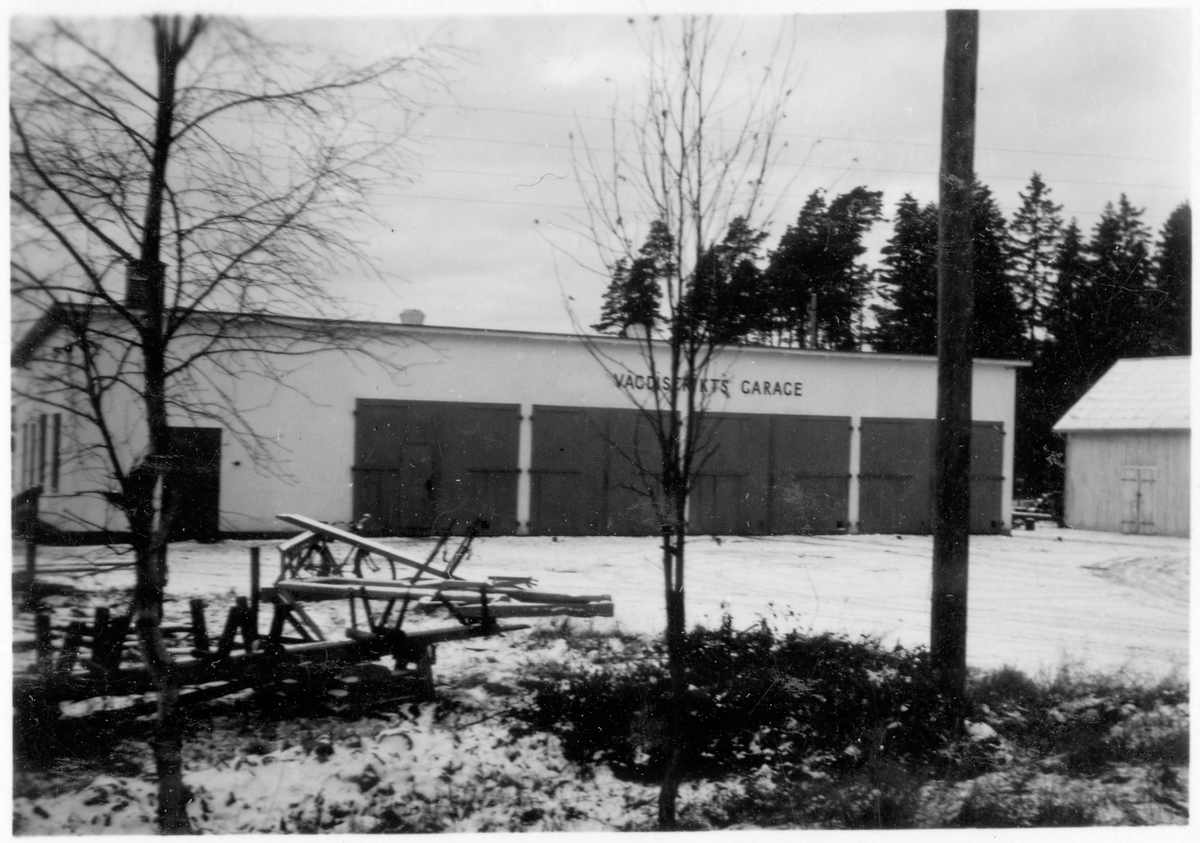 Vägstation E12, Tjällmo. Garagebyggnad, ovanför portarna texten "VÄGDISTRIKTETS GARAGE". Förrådsbyggnad till höger. 