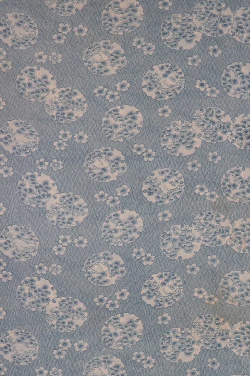 Blått trykk på hvit bunn, der større, hvite felt med sirkelform glir i hverandre, eller holder avstand, som vannliljeblader på vann. Disse feltene er fylt med små "grener" av nåletrær og tettstilte bølgeformasjoner, og mellom sirklene sees strøblomster, alt mot et tett bunnmønster av "labyrinter". Iflg. revidert katalogisering 1972, nevnes det kinesisk motivbruk, men en inspirasjon fra Japan virker mer innlysende. Etter utlån, er tekstilet nå innrammet bak glass, og vanskelig tilgjengelig for materialsjekk. Det nevnes på arkivkortet at det er en kypervevd flanellskvalitet.