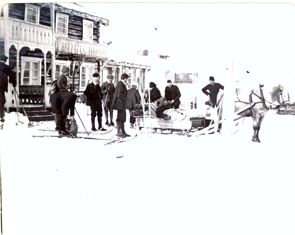 En gruppe skigåere gjør seg klar til å gå fra Bessheim til Randsverk, nesten seks timer i 33 minusgrader. Appelsiner og selters frøs i sekkene. I hestesleden sitter en skigåer med benbrudd. Fotografert i mars 1908.
