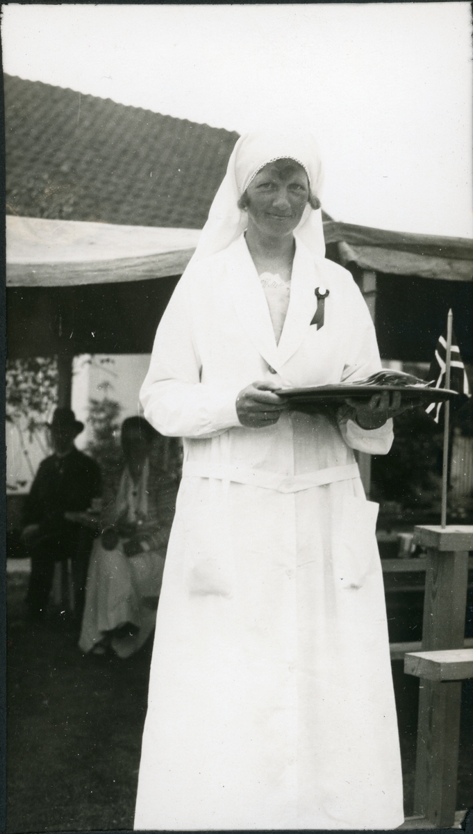 Ukjent kvinnelig kokk står med et brett foran provisorisk kjøkken under en folkefest på jaktslottet Malungen 22. Juni 1924. Bak skimtes flere medhjelpere.