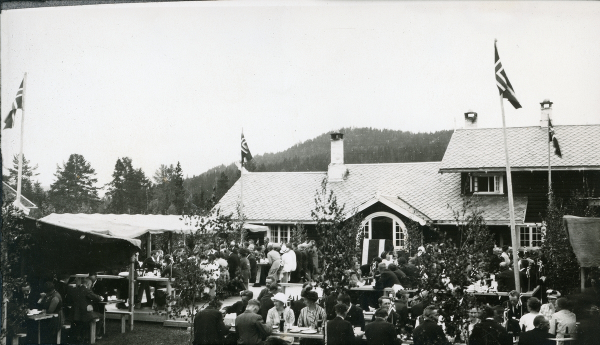 Folkefest på jaktslottet Malungen 22. Juni 1924. Gjestene sitter ved langbord på gårdsplassen. Til venstre et improvisert kjøkken med teltduk på taket.