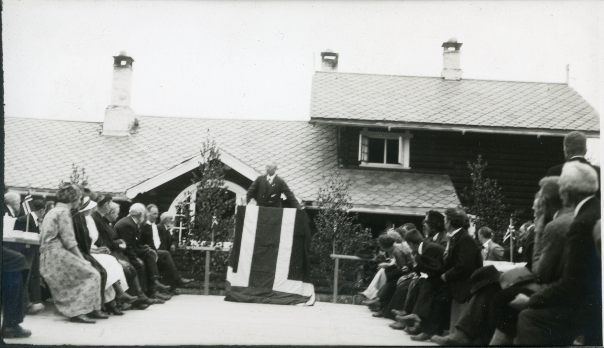 Folkefest på jaktslottet Malungen 22. Juni 1924. Westye P. Egeberg taler fra en improvisert talerstol på gårdsplassen. Tilhørerne sitter på benker.