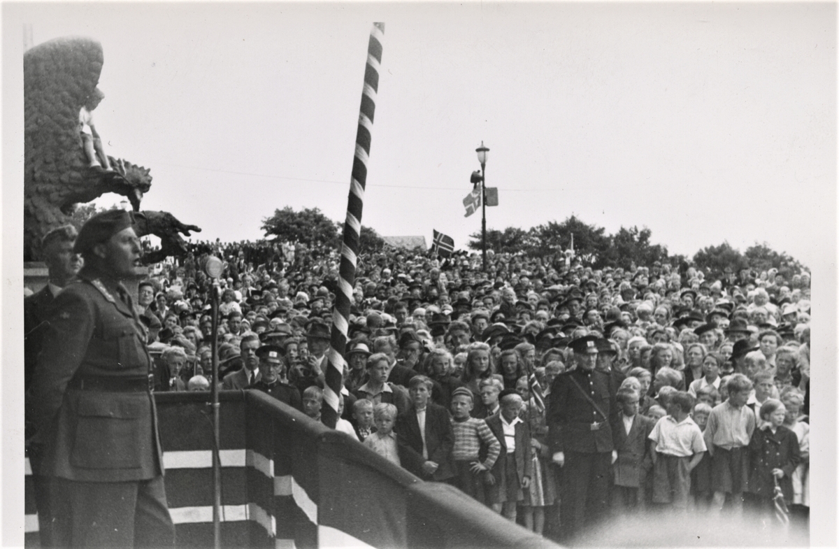 Norges Forsvarssjef kronprins Olav ankommer Haugesund Olsokdagen 29. juli 1945. Her er Kronsprinsens tale til folkemassene fra scenen på Rådhustrappen dokumentert. Bak kronprinsen ser vi ordfører Christian Haaland. Foran folkemengden ser vi politikonstabel Rydland.