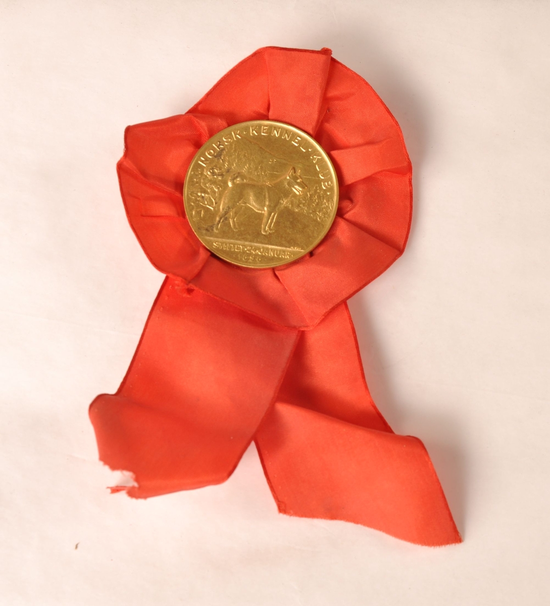 Rosett av rødt tekstil med medalje av gullfarget metall i midten