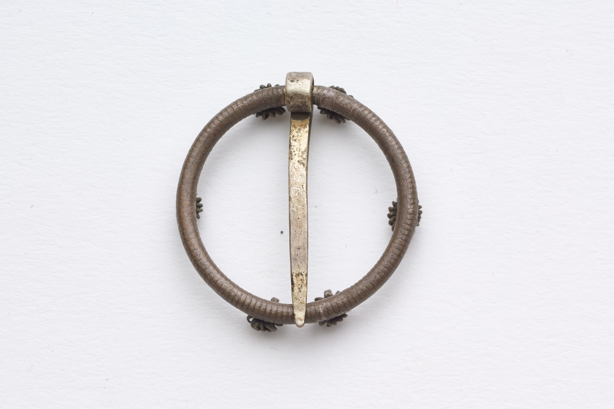 Spenna har form som en ring med små filligramsrosetter. Spenna har ei tverrgående festenål.