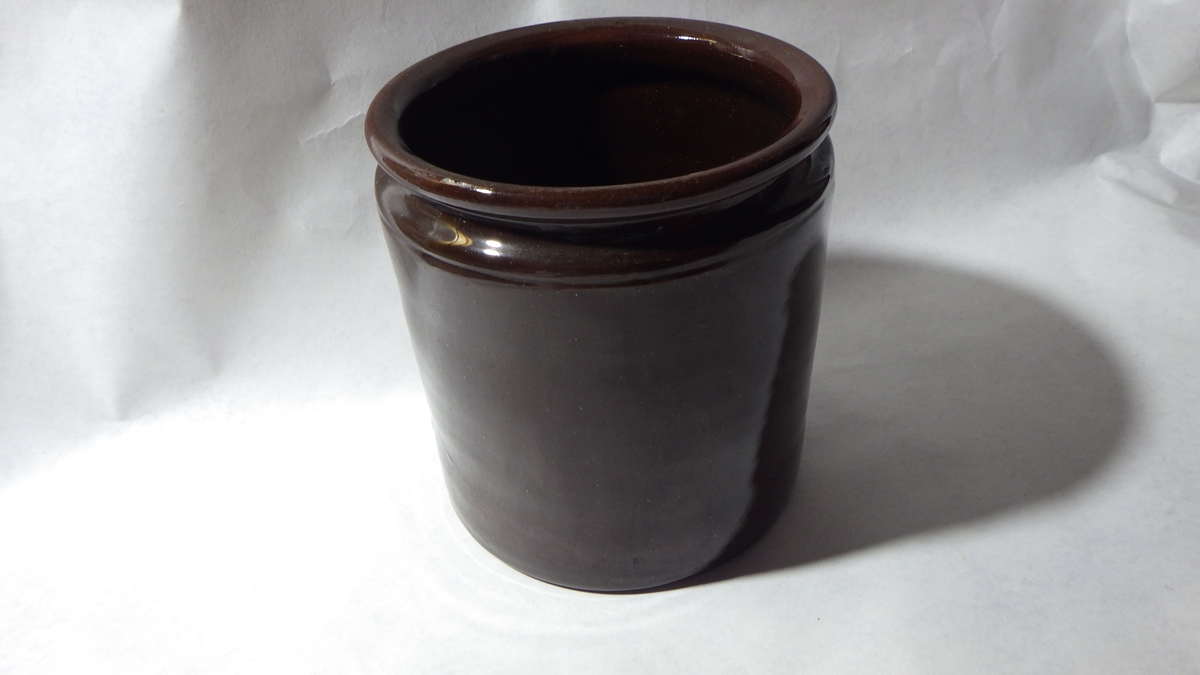 Leirgods, utvendig og innvendig brun glassur. Sylinderformet, inntrukket munningsrand.
