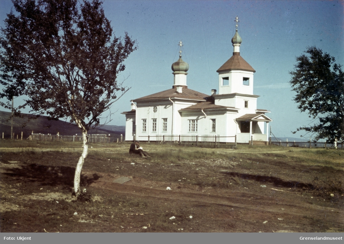 Kirken i Petsjenga, Parkina. En kar sitter i gresset foran kirken og ser i noen papirer.