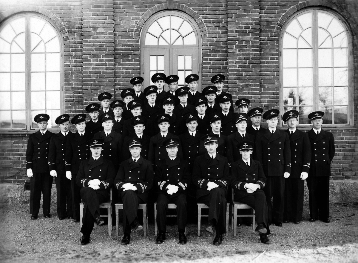 Gruppporträtt av 35 män i flygvapenuniform framför tegelbyggnad, den 21 december 1939. Mannen längst fram i mitten är Lage Thunberg, dåvarande chef för flygvapnets kadettskola.