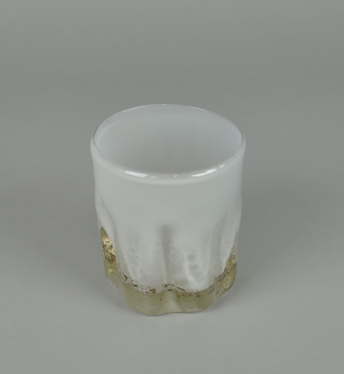 Munnblåst glassvase. Rund sylindrisk form, med bølgete innfellinger nederst på vasen. Hvit farge, med brunfarget dekorativ spiral.