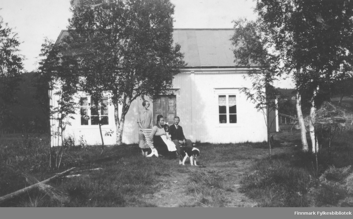 Fra venstre: Agnes Øksendal, fru og herr Øksendal sitter på benken, ei lite jente sitter mellom dem. En hund foran personene. Bildet er fra Mosjøen. Se også FBib.06031-001 og FBib.06031-018.