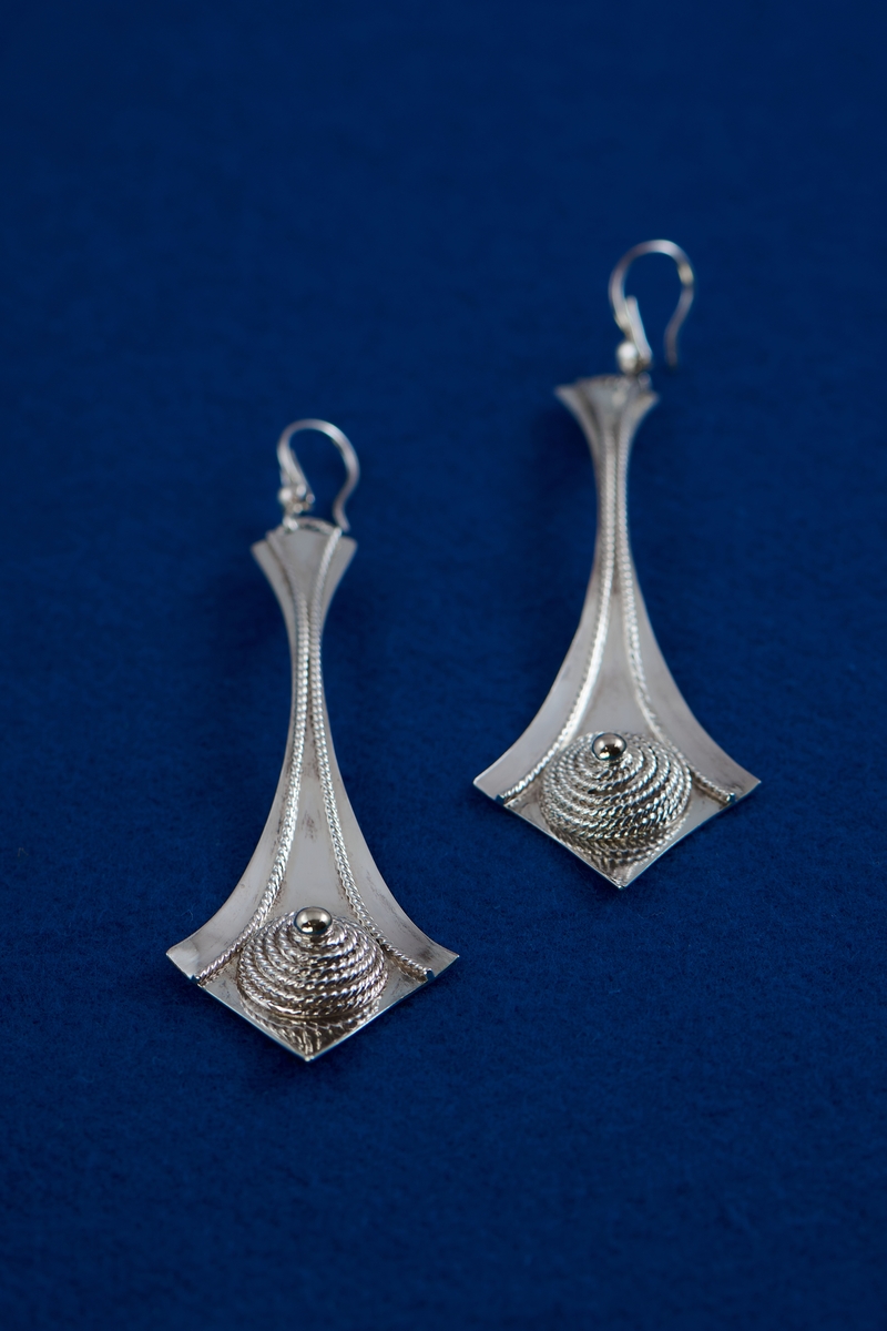 Örhängen i silver tillverkade av Rosa Taikon. De är dekorerade med en för Taikon karaktäristisk form: en spiral av filigrantråd omgärdar en minimal granalie av guld i spiralens mitt. De två örhängena har olika årsstämplar: F10 för 1980 respektive B11 för 2000.