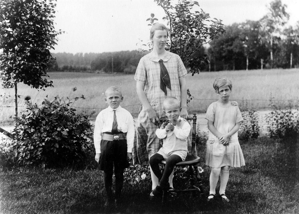 Kvinna med två pojkar och en flicka i trädgården. Eventuellt Bergstena socken.
