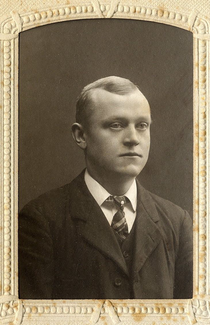 En ung man i mörk kostym med väst och slips med slipsnål. 
Bröstbild, halvprofil.
