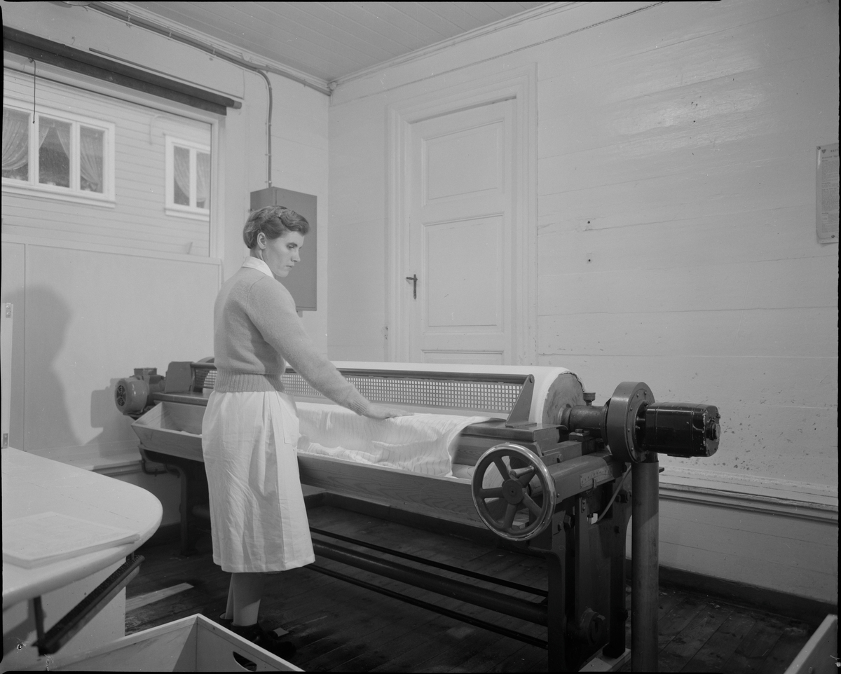 En kvinne ruller tøy med en elektrisk klesrulle på et vaskeri i Eigersund.
