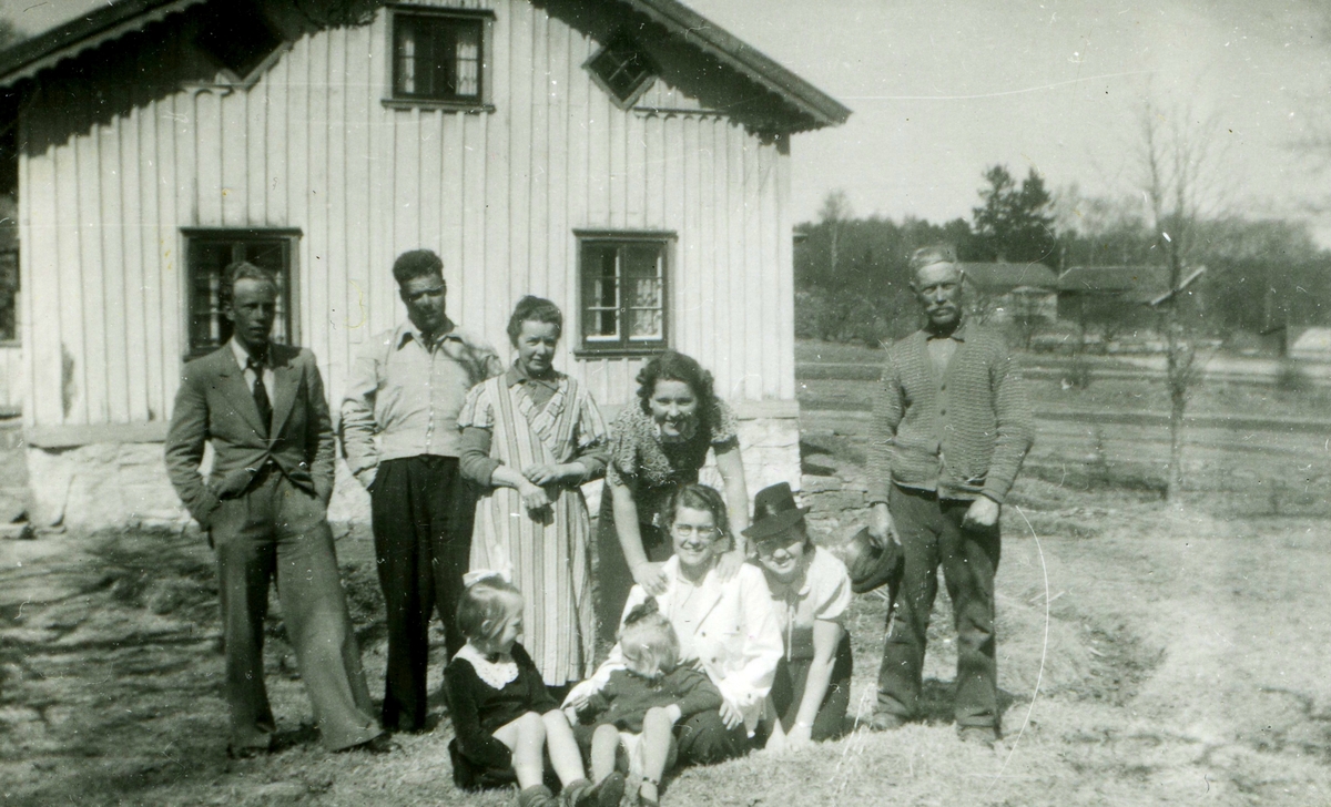 Några personer står utanför Sporred 1:8 "Fredriks", okänt årtal. Till höger syns gården "Brunos" med dess växthus. Tredje personen stående från vänster är Gerda Larsson (1880 - 1981). Stående längst till höger: Fredrik Larsson (1874 - 1961). Sittande, tredje person från vänster: Estrid Larsson (1912 - 1999, gift Karlberg). Övriga är okända.