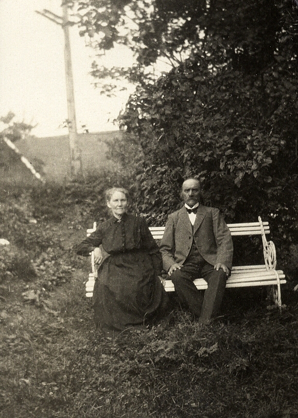 Ett äldre par sitter på en trädgårdssoffa i en trädgård.