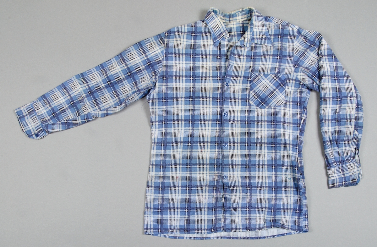 Skjorta av blå- och vitrutig bomullsflanell, maskinsydd, en bröstficka. 
