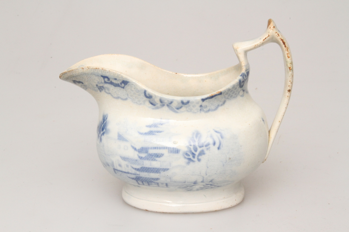 Mugge med blått Kina-inspirert mønster. Formen er oval, og tuten er nebbformet og bred. 