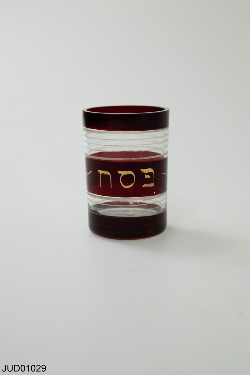 Litet glas för högiden pesach med röd bård och text på hebreiska.