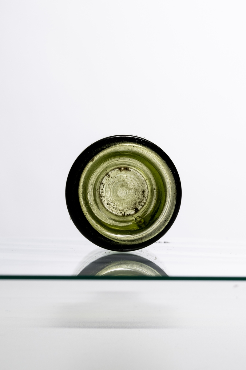 Brännvinsflaska av ljust grönt glas (mindre storlek), avsedd för tillslutning med naturkork. Flaskan har "Kinnekullebotten" med liten kula. Blåsor i glaset. Hantverksmässigt tillverkad vid Sunds glasbruk, Jönköpings län. Se vidare Historik.